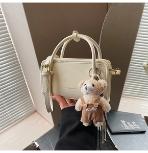 Detail of cream crossbody bag with leather texture and cute brown teddy bear charm