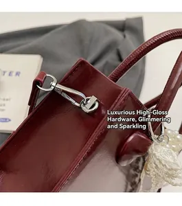 Close-up of wine red glossy leather handbag with silver hardware and pearl lace charm