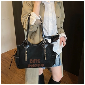 Detail of black suede tote bag with brown CUTE PUPPY embroidery and metal rivet accents