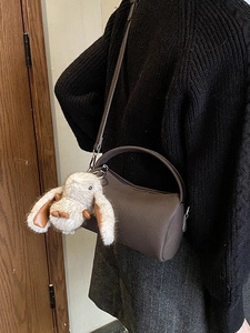 Dark brown leather cylindrical crossbody bag with cute plush rabbit charm on model
