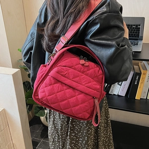 Detail of red quilted crossbody bag with wide strap and metallic hardware in casual use