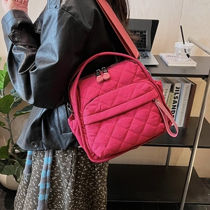 Detailed view of magenta quilted shoulder bag with diamond stitching shown on a model