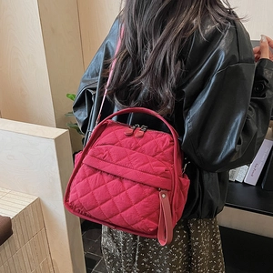 Detailed view of red quilted nylon bag with diamond patterns worn by a model