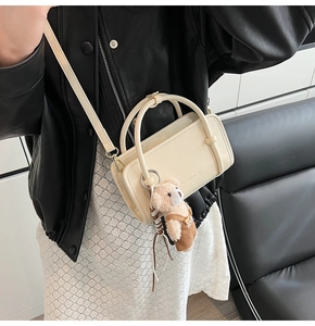 Detail of cream glossy mini handbag featuring a cute teddy bear charm and crossbody strap