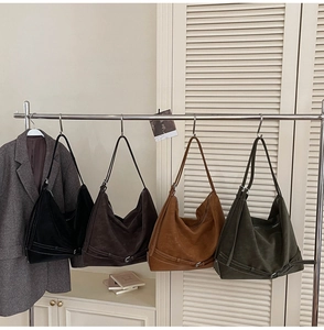Detail showing four suede hobo bags in assorted colors hanging on a minimalist rack