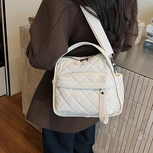 Detail of white quilted puffy shoulder bag with double zippers and wide strap on model