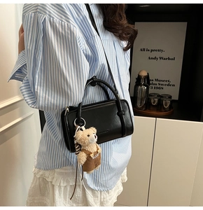 Detailaufnahme einer schwarzen Ledertasche mit süßem Teddybär-Anhänger an der Seite