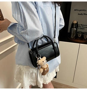 Detail of black mini crossbody bag with a cute teddy bear charm on blue stripe shirt
