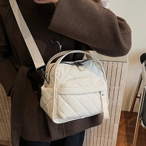 White quilted nylon crossbody bag with wide strap shown on a model with brown coat