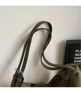 Detail of adjustable long shoulder strap with metal buckles on an olive green suede tote