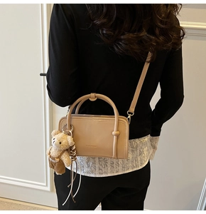 Detail of a beige leather crossbody bag with circular handles and a cute bear pendant