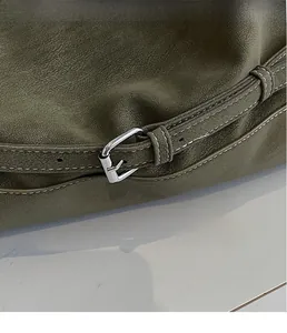 Detailed macro view of dark green pebbled leather tote with silver buckle and white stitching
