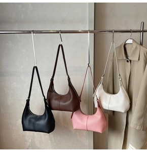 Four crescent moon underarm bags in black, brown, pink, and white on a metal rack
