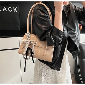 Detail of beige patent leather handbag featuring bow ribbon and pearl chain accents