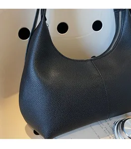 Close-up of black lychee grain leather underarm bag with silver zipper and curved silhouette