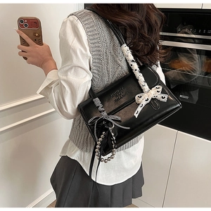 Détail du sac à bandoulière noir avec nœuds en dentelle blanche et motif à carreaux