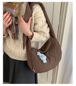 Detailed view of brown quilted puffer shoulder bag with wide strap and blue pendant