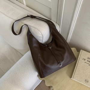 Detail of dark brown tote bag with leather texture and metal buckle on white sofa