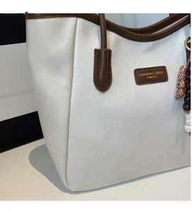 Detail of off-white tote bag with dark brown leather trim and retro beaded tassel charm