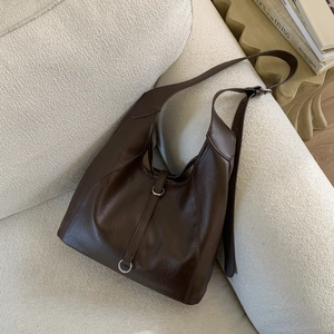 Detail of a large dark brown hobo shoulder bag in shiny leather on a beige sofa