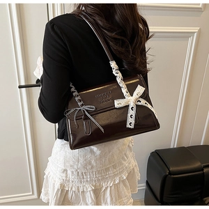 Detail of dark brown patent leather shoulder bag with chic lace and plaid bow accents