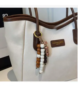 Close-up of white tote bag featuring brown leather trim and decorative wooden beads