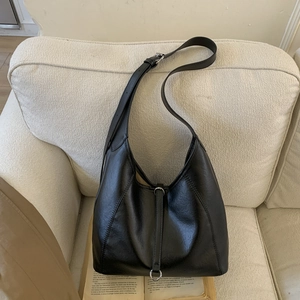 Close-up of black leather tote bag with silver buckle detail on a white sofa