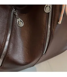 Détail du sac en cuir marron foncé montrant les fermetures éclair et la texture souple