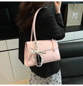 Detail of pink faux leather shoulder bag with embossed letters and bow chain accessory