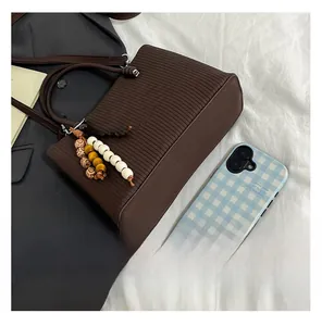 Detail of dark brown tote bag with vertical stripes and a colorful beaded tassel charm