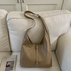 Detail of tan brown hobo tote bag with metal ring decoration on white sofa