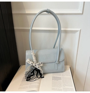Detail of light blue glossy leather envelope bag featuring a lace bow and metal bead charm