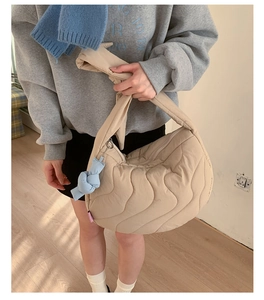 Detailed view of beige quilted crescent shoulder bag with a stylish blue knot charm