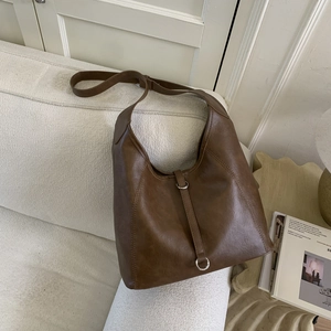 Close-up of dark brown leather tote bag on white sofa with vertical stitching and metal ring