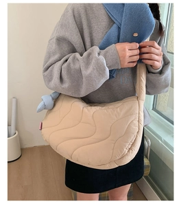 Detail of beige quilted dumpling bag featuring wavy stitching and blue knot accessory