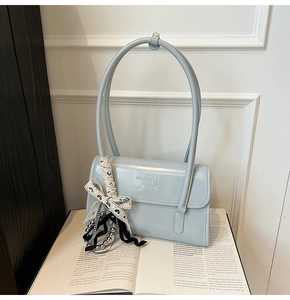 Close-up of light blue leather shoulder bag with embossed logo and elegant ribbon charm
