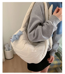 Close-up of white quilted puffer crossbody bag with soft padding and blue ribbon charm