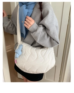 White quilted crossbody bag with wave texture and blue knot charm on a female model