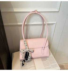 Pink shoulder bag with embossed texture and elegant lace bow charm on fashion magazine
