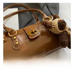 Close-up of brown glossy faux leather baguette bag with a golden metal twist lock detail