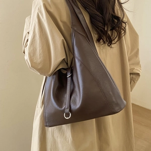 Detail of a dark brown minimalist tote bag with soft leather texture and silver ring accents