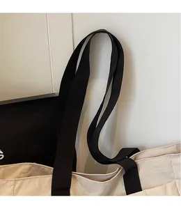 Detail of a minimalist off-white tote bag featuring wide black shoulder straps and stitching
