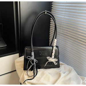 Détails d'un sac bandoulière noir brillant avec rubans en dentelle et nœud chic