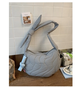 Close-up of gray quilted crossbody bag with knot strap detail and fashion tag