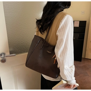 Detail view of large brown tote bag with decorative beads and vintage leather logo