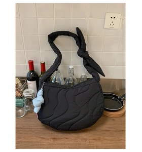Detail of black wave-quilted shoulder bag with blue fabric knot pendant on a counter