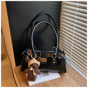 Detail of glossy black shoulder bag with gold hardware and a cute knit bear charm