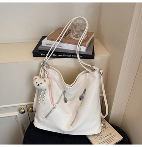 Détail d'un grand sac hobo crème avec fermetures éclair et pendentif ours en peluche