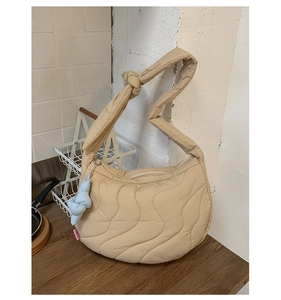 Close-up of beige quilted dumpling bag with knotted strap and light blue fabric pendant