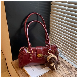 Detail of dark red glossy leather shoulder bag with cute teddy bear charm on wood surface